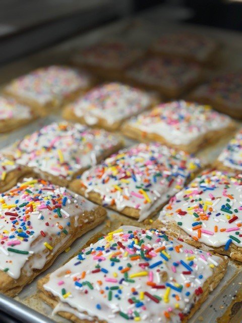 A baking tray of homemade pop tarts topped with white icing and rainbow sprinkles.