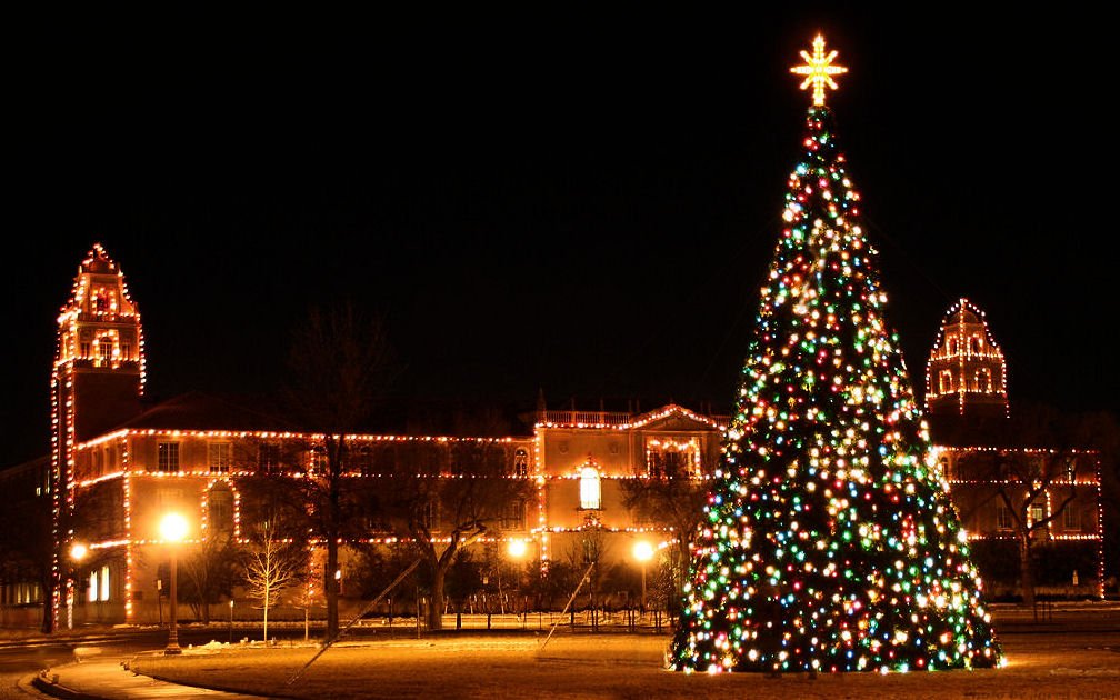 Texas Tech's campus buildings outlined in thousands of red, white and orange lights at night, with a towering multicolored Christmas tree topped by a lighted star