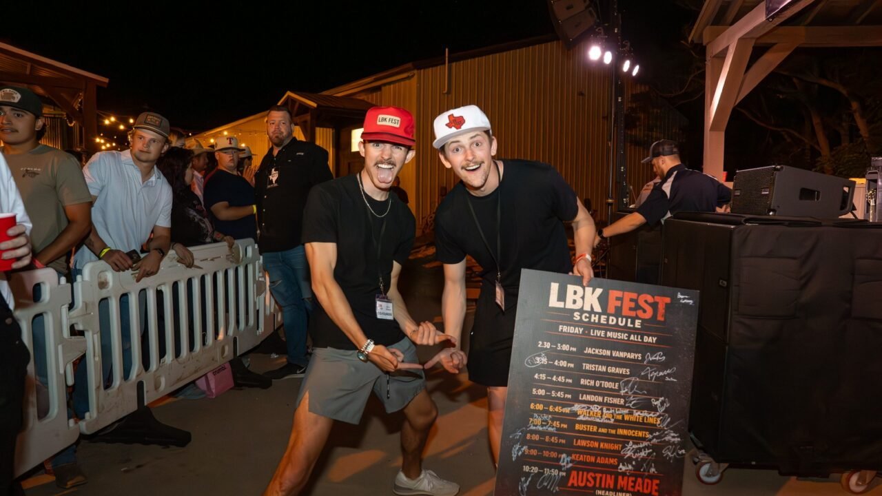 LBK Fest co-founders Bryson Callaway, left, in a red LBK Fest cap, and Bryce McClaugherty, right, in a white cap, point at the LBK Fest schedule board signed by the performers.