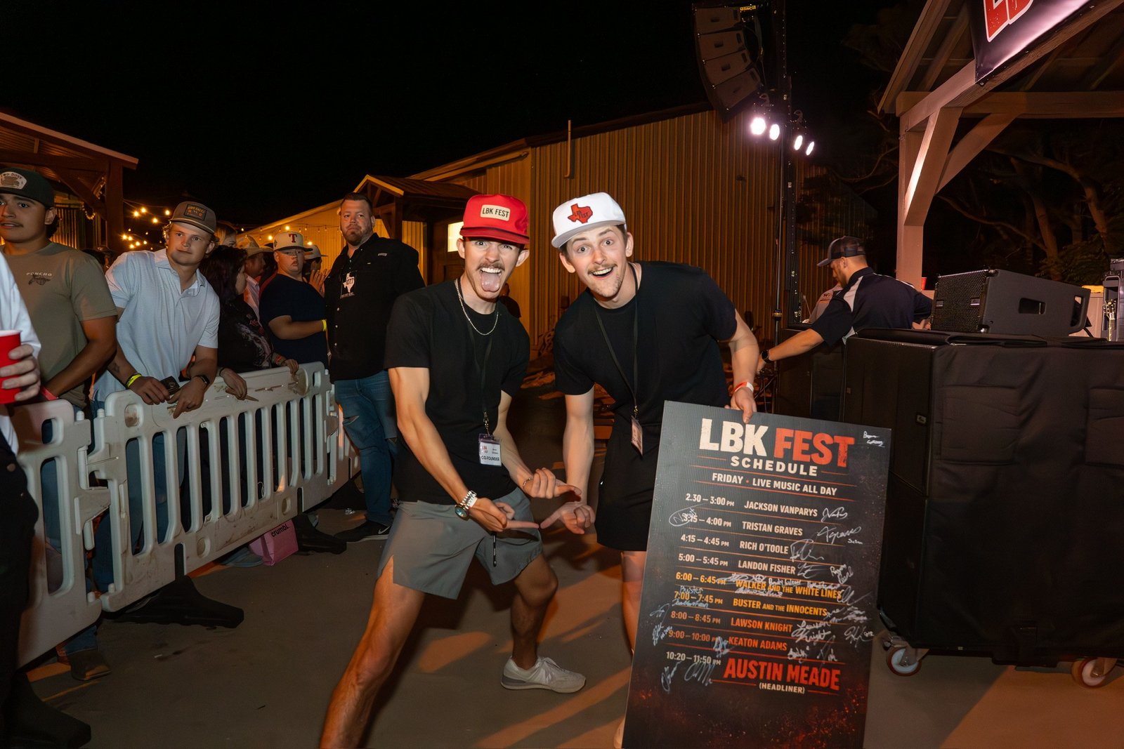 LBK Fest co-founders Bryson Callaway, left, in a red LBK Fest cap, and Bryce McClaugherty, right, in a white cap, point at the LBK Fest schedule board signed by the performers.