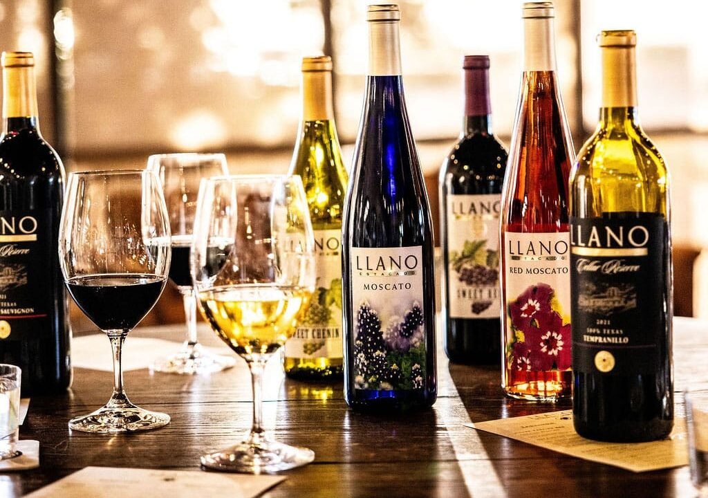 A lineup of Llano Estacado Winery wine bottles and filled glasses on a wooden tasting table.