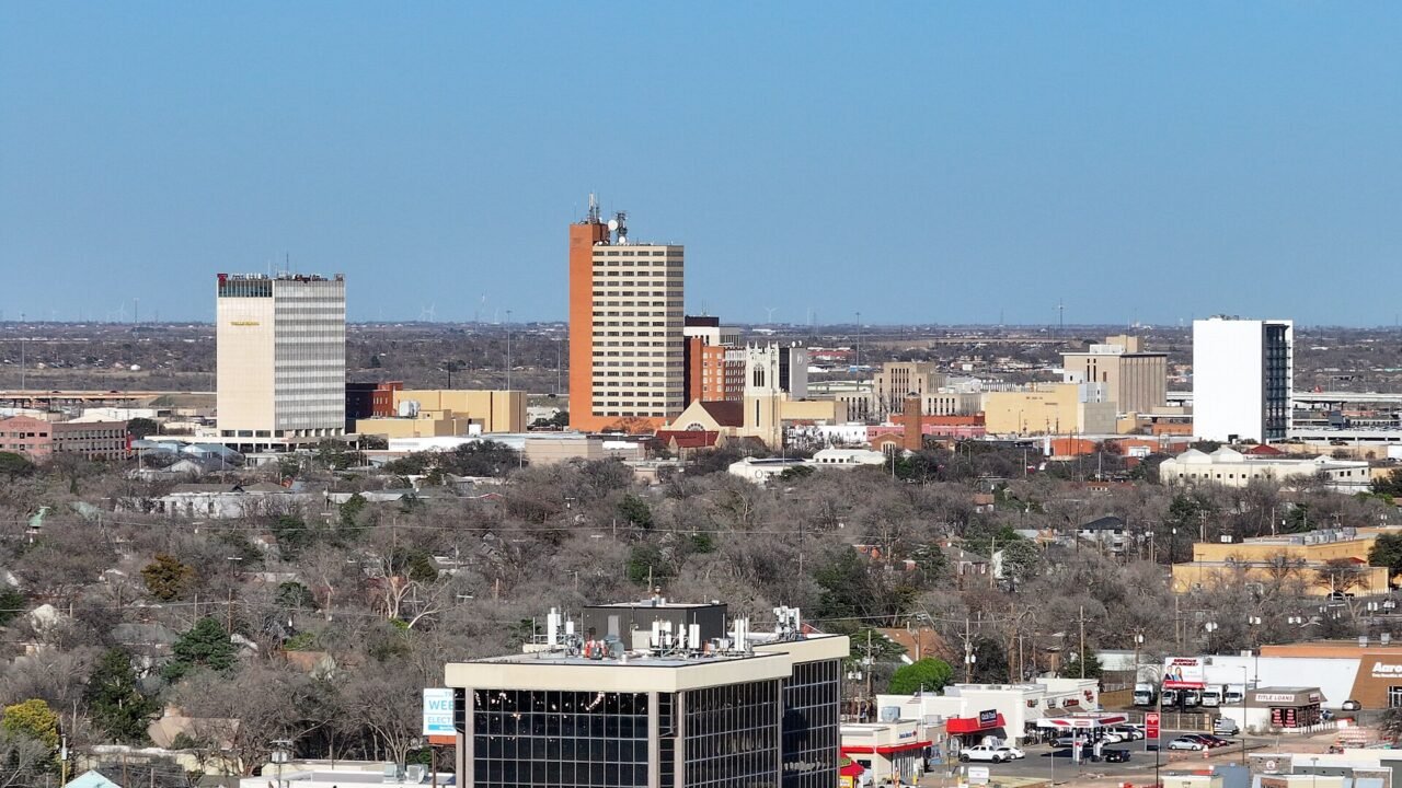 Downtown Lubbock skyline with tall office towers rising above tree-lined neighborhoods under a clear blue sky