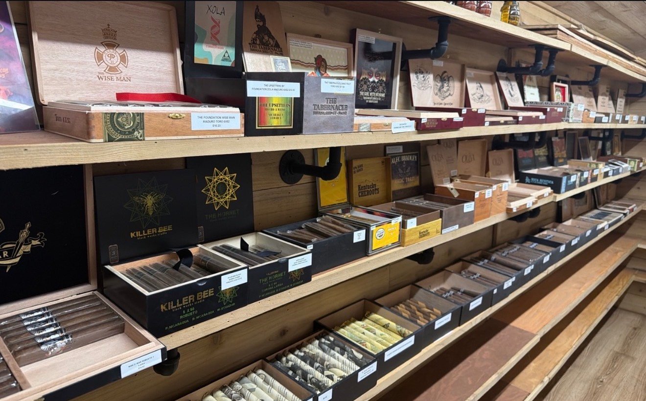 Inside the walk-in humidor at Mystery Shack Cigars & Coffee, where wooden shelves hold rows of boxed premium cigars from several brands.
