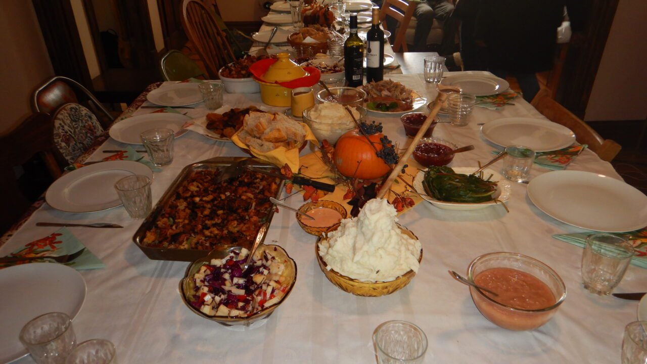 A Thanksgiving table set with stuffing, mashed potatoes, cranberry sauce, green beans and a small pumpkin centerpiece